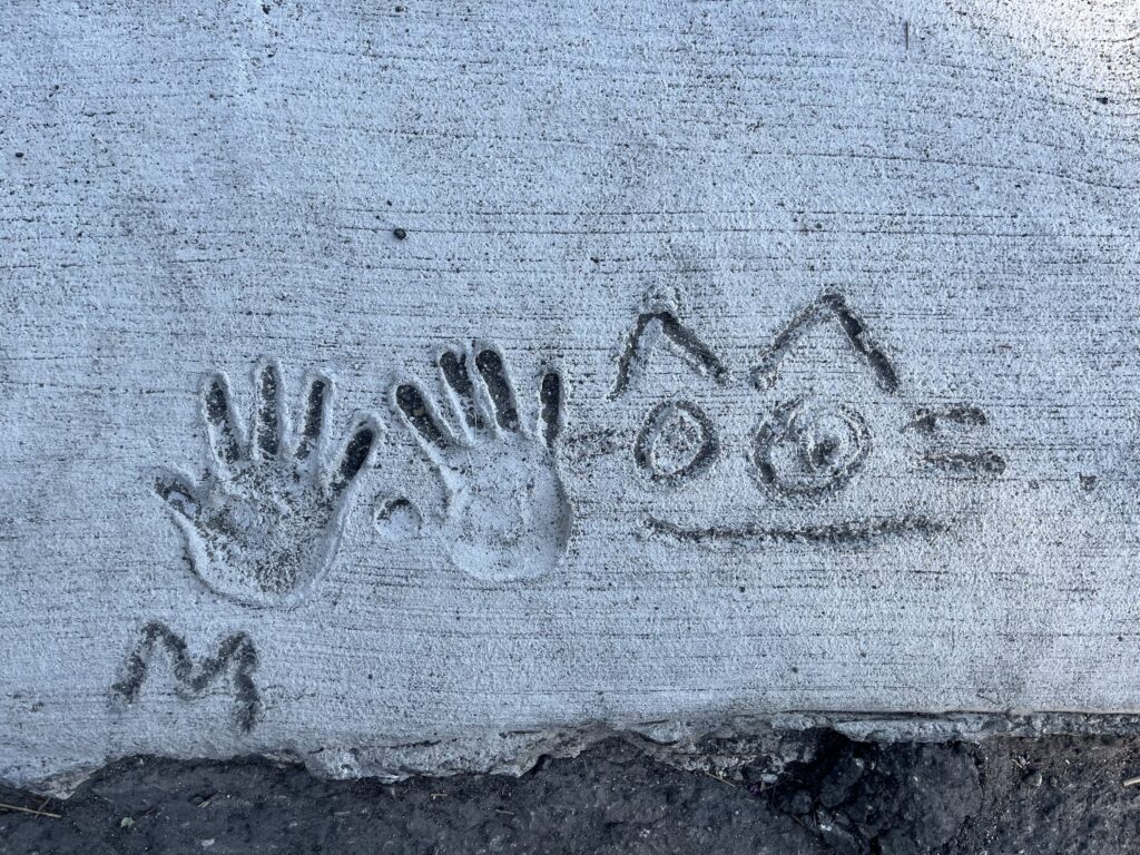 A sketch of a cat with two handprints etched in wet cement.